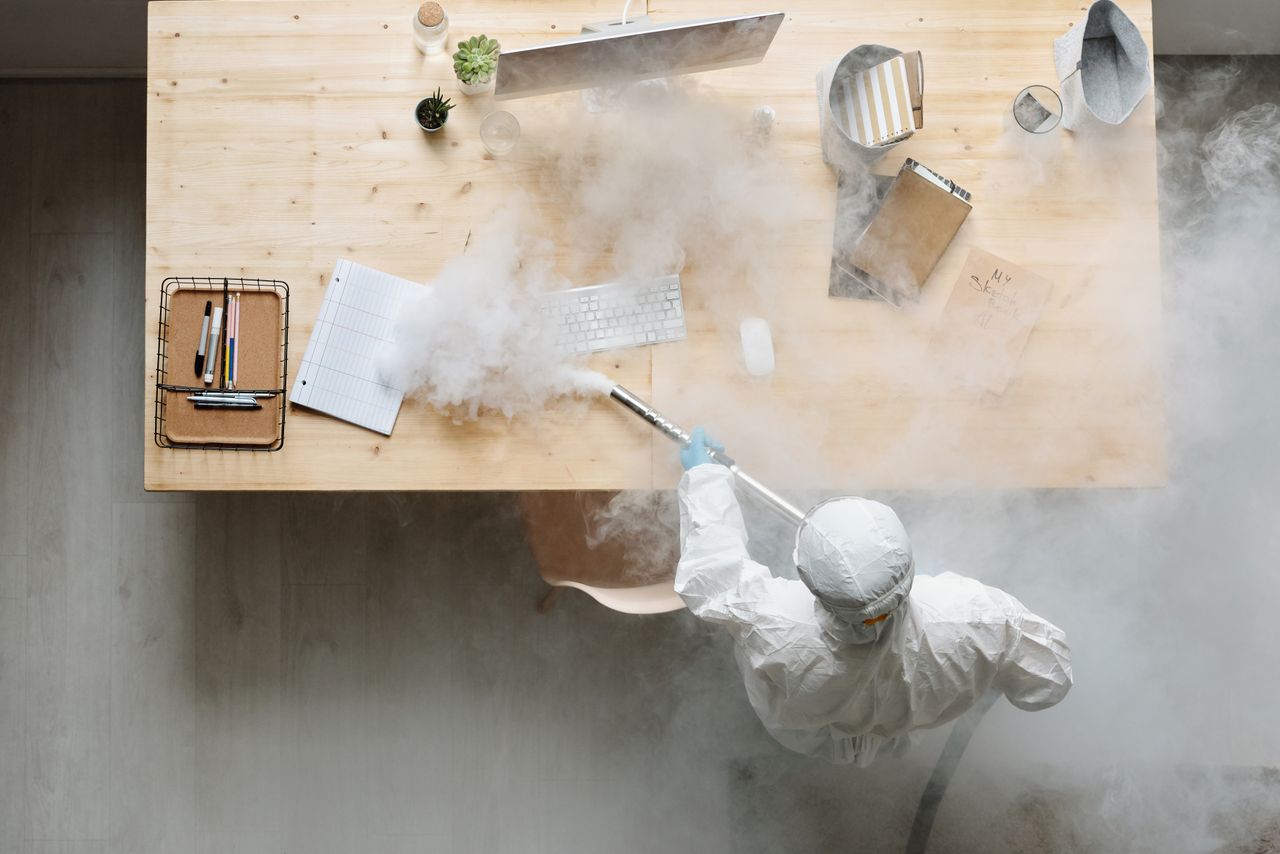 Une personne désinfecte un espace de travail par fumigation, en portant un équipement de protection complet pour sa sécurité.